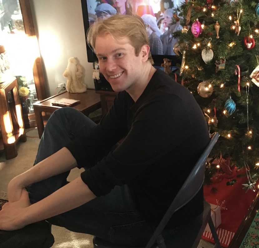 Image of Alex Rubin sitting next to a Christmas tree